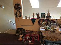 Wide shot showing several wreaths, decorative trees in gold and glass, metal and glass candle holders, gold garland, and holiday trays arranged on table and wall.