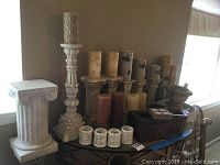 Wide view showing various pillar candles, votive holders, decorative boxes, and pedestals with faux sandstone and granite finishes on table near window.