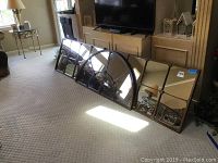 Three large 24x48 mirrors leaning against a fireplace, including two rectangular and one half-circle mirror with metal frames reflecting the living room.