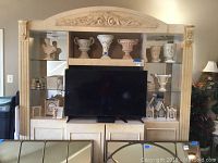 Front view of the entertainment center showing carved resin and wood construction, mirrored back, shelves, and closed cabinets beneath.