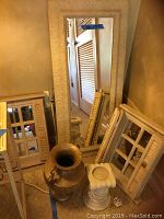 Photo showing two wood shutter style mirrors, tall rectangular carved resin mirror behind them, metal urn and resin candle holder in front