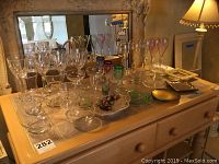 Wide view of dresser with arranged crystal wine glasses, colored tulip glasses, cordial glasses, and vases