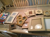 Various resin, wood, and stone picture frames displayed on a table along with marker sets, scrapbook paper, and a coloring book.