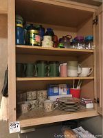 Cabinet with various plastic jugs and mugs on upper shelves, floral patterned cups and saucers on pull-out surface.