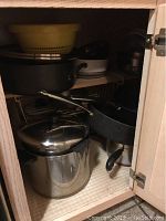 Cabinet with stacked KitchenAid non-stick pots and pans in black, stainless steel pot, and other cookware.