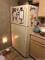 Full side and front view of off-white Whirlpool Gold refrigerator with freezer on top, located in kitchen near wooden cabinetry and floor tiles.