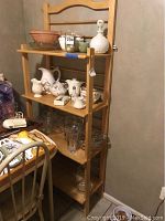 Side angled view of the wood bakers rack loaded with ceramic and glass kitchenware items showing four shelves.