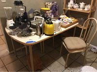 Photo of kitchen table with white Formica top and four metal chairs with cushioned seats, cluttered with kitchen items (not included).