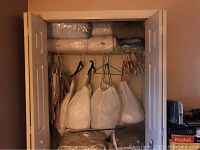 Closet interior with multiple cloth bags hanging and mattress pads folded on shelf, showing storage and quantity