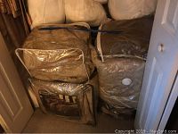 Closet floor packed with large bags of bedding, including comforters, pillows, blankets, and mattress pads.