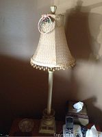 Tall decorative lamp with textured fabric shade and gold-tone beaded trim along bottom edge, approximately 31 inches tall