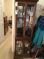 Full view of closed wooden curio cabinet with glass front doors showing five shelves inside.