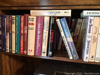 Photo of one shelf of assorted paperback and hardcover books including titles like 'Jackie Collins', 'Prison', 'This Calder's War'