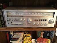 Silver-face Lloyds AM FM stereo receiver sitting on wooden shelf with books behind it