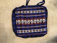 Blue handbag with horizontal stripes and central band of intricate embroidery in red, white, and black.