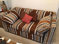 Front view of mid century style sofa with striped brown and tan upholstery along with cushions