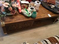 Wide angle photo showing the front and top surfaces of the rectangular coffee table with metal corner accents, sliding door with textured design, various items on top