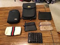 Various small purses and wallets including a black leather handbag, black coin purses, beige fabric purse, and a black textured wallet on a wooden table.