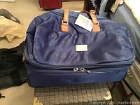 Large navy blue expandable rolling duffle bag with leather handles and a JM New York brand plate on the front.