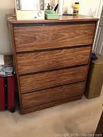 Full view of wooden chest of drawers, showing four drawers with dark inset handles and brown wood grain finish