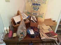 Top view of cabinet showing basket, Nortex chair pad, papers, small containers, and boxes with sewing supplies on the cabinet surface.