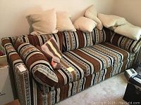 Full view of a striped brown, black, beige, and white patterned sofa with five matching pillows on a light carpet.