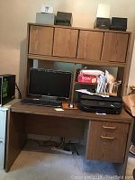 Front view of wooden desk with computer monitor, keyboard, printer, and hutch with four cabinet compartments. Six storage boxes on top of hutch.