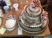 Overview of tureen and ladle rest on table among other items. Shows full tureen with lid and underplate plus ladle rest to left.