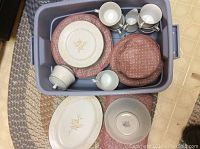 Top view of all porcelain pieces including plates, cups, creamer, sugar bowl placed inside plastic bin with soft pads.
