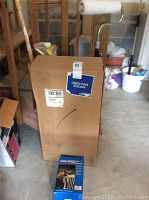 Boxed Campbell Hausfeld spray gun and paint roller covers next to furniture and other stored items in garage.