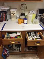 Top counter with Osterizer blender, Sunbeam Hot Shot kettle, plastic containers, mugs, and cups. Shelves with books on the left side.
