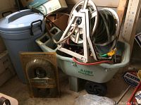 Photo showing Ames Easy Roller Jr. plastic lawn cart with garden hose reel and three garden hoses inside cart next to Rubbermaid trash can and window air conditioner vent.