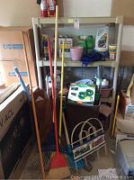 Plastic shelving unit with assorted cleaning supplies and garden tools in front