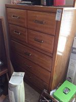 Front view of wooden 5 drawer chest with metal handles and medium brown finish, showing some wear and seller's label on top right corner.