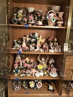Full front view of four shelves filled with porcelain floral and figurine pieces in a wooden shelving unit.
