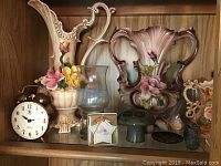 Porcelain vases with floral designs, vintage clock, glass candle holder, small ceramics.