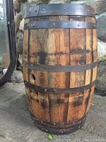 Side view of the oak wine barrel showing wooden slats and metal bands, with some wear and a hole on one side.