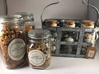 Photo of 3 large glass jars with metal clasp lids and a metal crate with wooden handle containing 4 smaller jars with cork lids