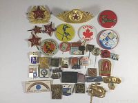 Photo shows an assortment of pins and buttons including red star badges, Soviet military style pins, city sketches, and multiple colorful souvenir buttons.