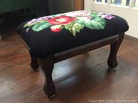 Overall angled view of the footstool showing the floral needlepoint upholstery and wooden legs