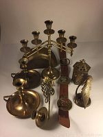 Wide view showing multiple brass items including candleholders, belt with medallions, lantern, and brass crane figurine