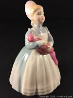 Front side view of Royal Doulton figurine THE RAG DOLL holding a pink rag doll, dressed in blue and white dress with bonnet.