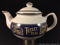 Front angle view of the white ceramic Tetley Teas teapot showing the detailed navy blue and gold branding band and lid with matching decorative knob.