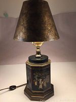 Full view of the lamp showing dark metallic textured shade, brass hardware, and hexagonal base with toleware painted Asian figures.