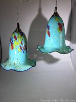 Front view of the pair of blue art glass ceiling lights showing their bell-shaped shades with colorful red, yellow, and blue spots and undulating edges.