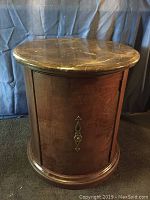 Front view of the wooden table showing the marble top and closed cabinet door with decorative metal handle.