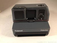 Front view of Polaroid Impulse camera showing lens, flash, and film ejection slot.