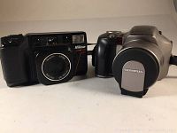 Both Nikon Tele Touch and Olympus IS 20 cameras side by side, showing black and silver bodies.