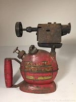 Side view of antique National Torches blow torch showing full item with red paint and rusted metal parts.
