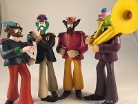 Four Beatles action figures from McFarlane Toys shown in Sgt. Pepper's band attire, standing with bands and posing.